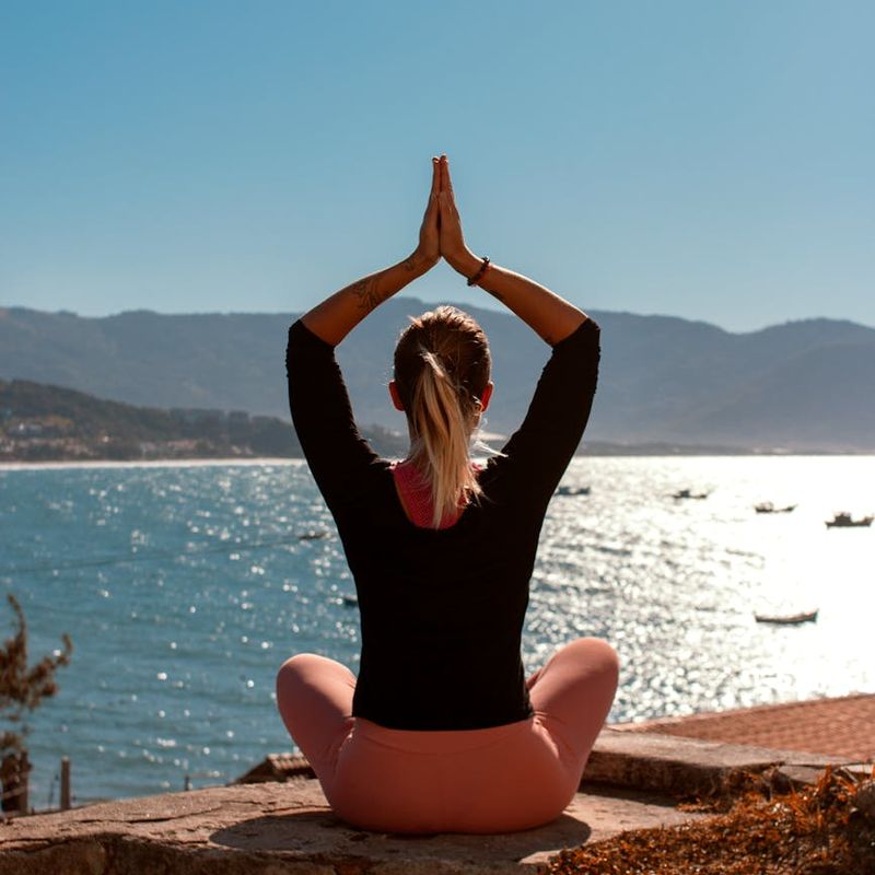 Woman in a peaceful yoga pose on a dock by the water at sunrise.
