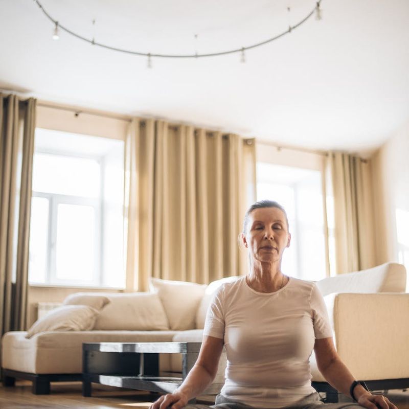 Woman with eyes closed, smiling gently, sitting on a yoga mat indoors.